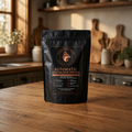 A black stand-up pouch of automatic dishwasher powder stands on a wooden kitchen counter with a blurred warm kitchen interior in the background. The front label shows the brand 'The Dish Supply Company' with a fox logo and product text in gold and white.