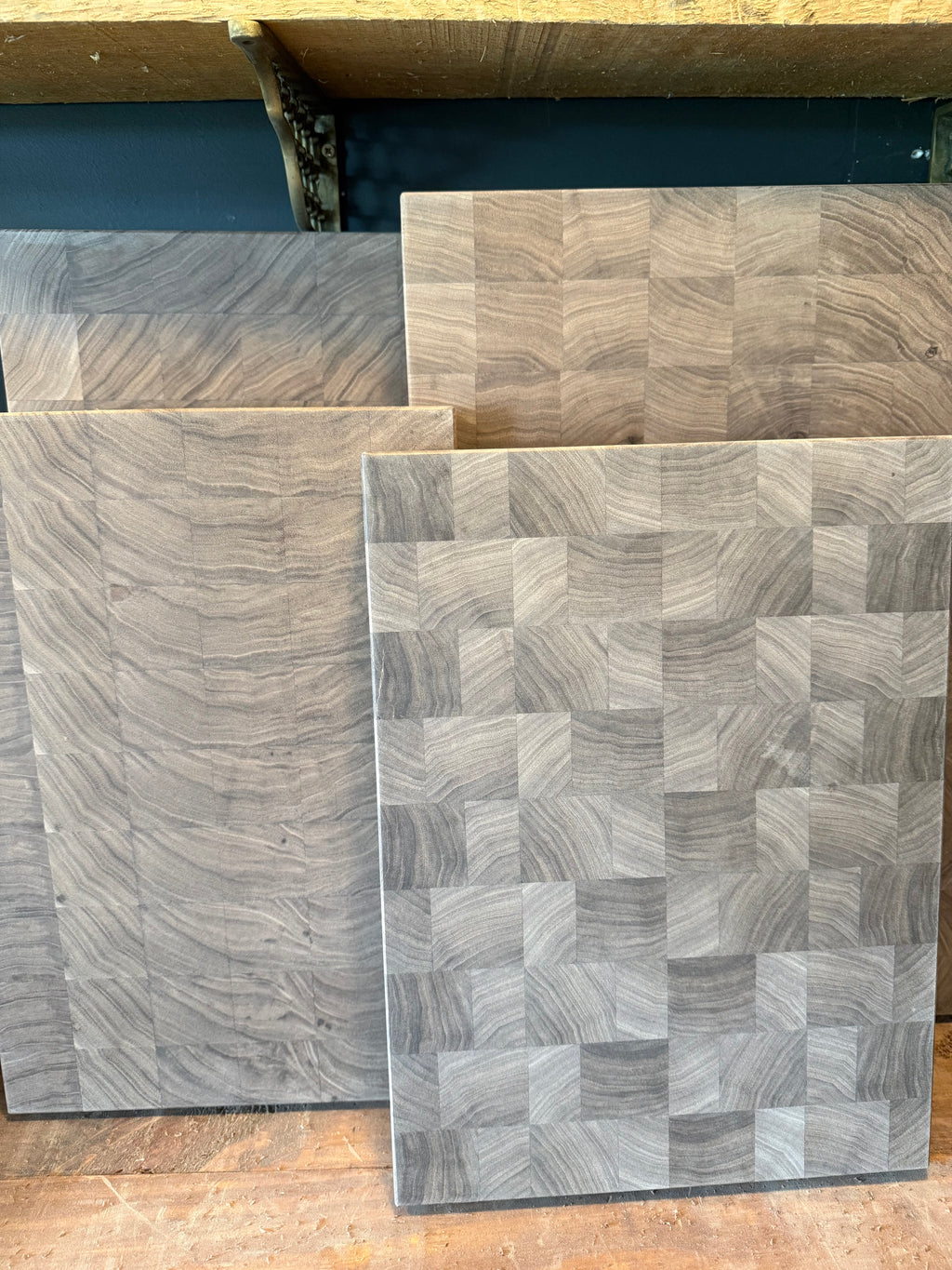 Four unfinished walnut cutting boards with different end-grain patterns standing upright in a woodworking shop.